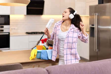 Foto de Joven feliz ama de casa mujer cantando y limpiando su casa, chica disfrutando del trabajo doméstico. - Imagen libre de derechos