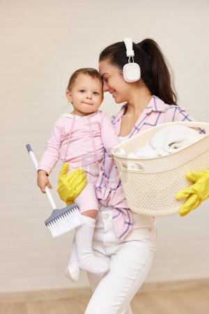 Photo for Happy mother housewife is holding cute little child girl and basket with laundry and doing housework , Happy family - Royalty Free Image