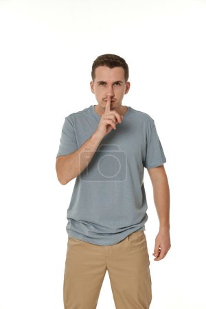 Téléchargez les photos : Jeune homme montrant signe de silence geste sur fond blanc - en image libre de droit