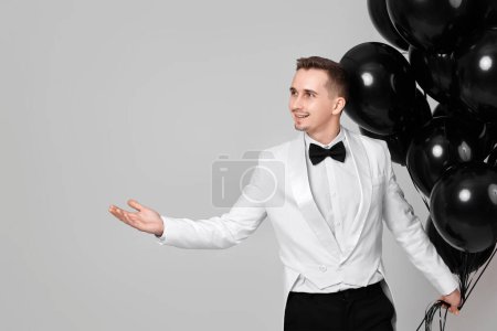 Téléchargez les photos : Élégant homme caucasien en costume blanc smoking avec ballons à air noir. espace de copie. Fête - en image libre de droit
