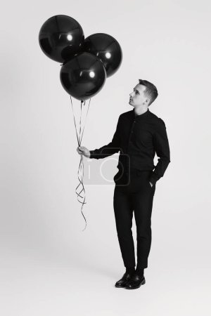 Foto de Elegante hombre caucásico con racimo de globos de aire negro sobre fondo blanco. blanco y negro - Imagen libre de derechos