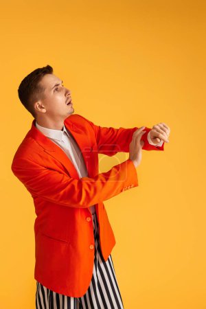 Foto de Joven alegre divertido en chaqueta naranja y pantalones a rayas sobre fondo amarillo vibrante. - Imagen libre de derechos