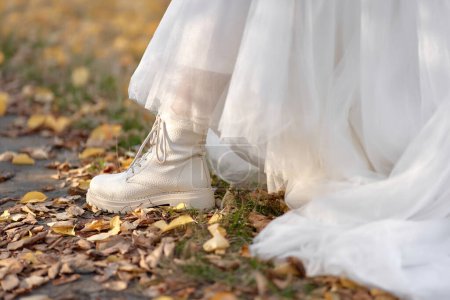 Téléchargez les photos : Mariée portant des bottes blanches et robe blanche est debout sur les feuilles d'automne. mariage d'automne - en image libre de droit