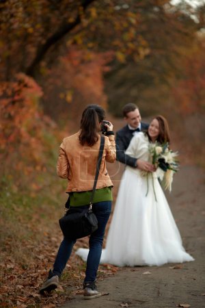 Photo for Female wedding photographer taking pictures of the bride and groom on the wedding day in autumn - Royalty Free Image