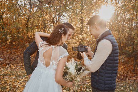 Foto de Fotógrafo de bodas muestra que acaba de tomar fotos a la pareja de boda. novia y novio en la naturaleza - Imagen libre de derechos