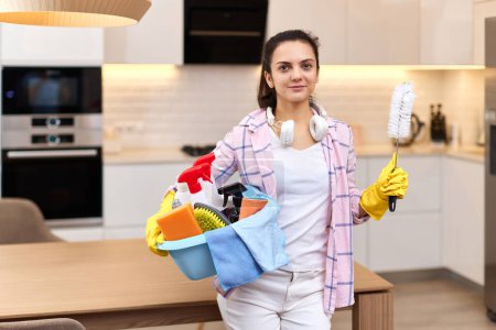 Foto de Mujer feliz en guantes protectores de goma amarilla sosteniendo herramientas de limpieza. tareas domésticas. - Imagen libre de derechos
