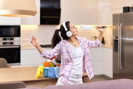 Téléchargez les photos : Jeune femme au foyer heureuse chantant et nettoyant sa maison, fille appréciant le travail domestique. - en image libre de droit