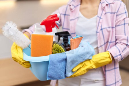 Foto de Mujer con guantes protectores de goma amarillos sosteniendo herramientas de limpieza. tareas domésticas. - Imagen libre de derechos