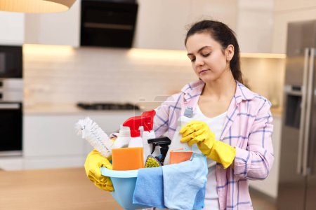 Photo for Woman in rubber protective yellow gloves holding bucket with cleaning detergents and rags . house chores. - Royalty Free Image