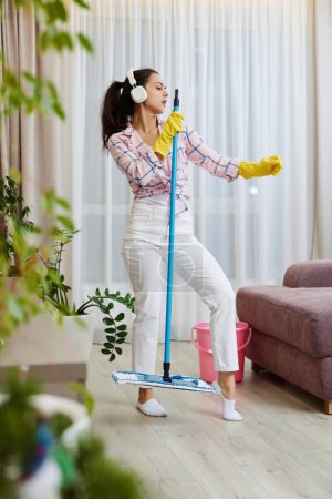 Téléchargez les photos : Femme heureuse chantant et lavant le sol dans le salon, tâches ménagères. - en image libre de droit