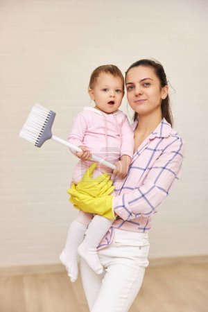 Téléchargez les photos : Mère heureuse femme au foyer tient bébé fille mignonne et faire des travaux ménagers à la maison, famille heureuse - en image libre de droit