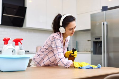 Foto de Mujer joven limpiando y limpiando mesa de madera con paño de microfibra. tareas en casa. Servicio de limpieza - Imagen libre de derechos