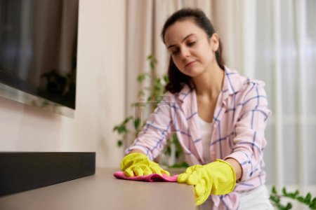 Foto de Mujer joven en guantes limpiando y limpiando mesa con paño de microfibra. tareas en casa. Servicio de limpieza - Imagen libre de derechos