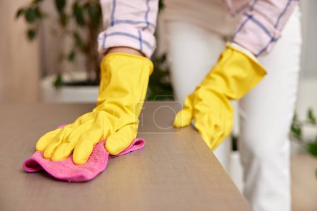 Téléchargez les photos : Jeune femme en gants de nettoyage et d'essuyage table avec chiffon en microfibre. corvées à la maison. Ménage - en image libre de droit
