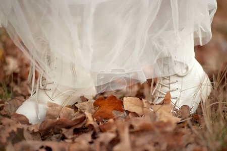 Foto de Novia con botas blancas y vestido blanco está de pie sobre hojas de otoño. boda de otoño - Imagen libre de derechos