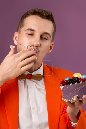 Téléchargez les photos : Bel homme anniversaire manger gâteau délicieux sur fond violet - en image libre de droit