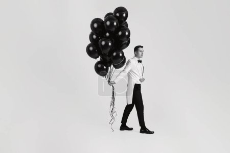 Foto de Elegante hombre caucásico en traje esmoquin blanco con globos de aire negro sobre fondo blanco. Longitud completa - Imagen libre de derechos