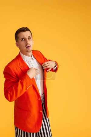 Téléchargez les photos : Jeune homme extravagant en veste orange et pantalon rayé sur fond jaune. - en image libre de droit