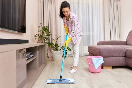 Téléchargez les photos : Femme nettoyage et nettoyage du sol dans le salon, ménage quotidien - en image libre de droit