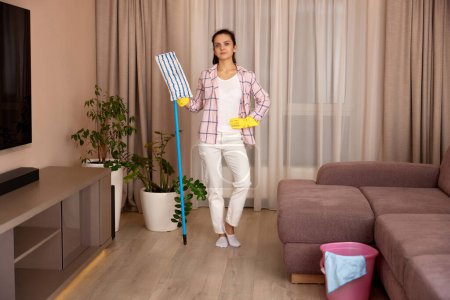 Photo for Young woman cleaning and mopping floor at living room at the evening, daily housekeeping - Royalty Free Image