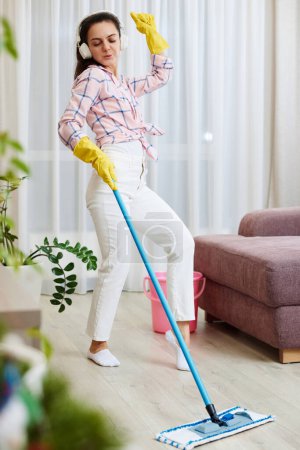 Téléchargez les photos : Femme heureuse chantant et lavant le sol dans le salon, tâches ménagères. - en image libre de droit