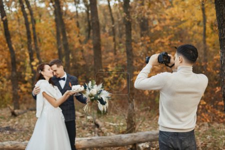 Téléchargez les photos : Photographe de mariage homme prenant des photos de la mariée et le marié dans la nature en automne - en image libre de droit