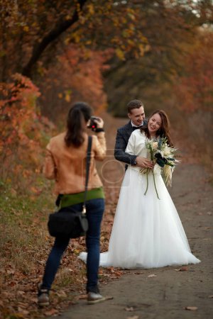 Téléchargez les photos : Photographe de mariage femelle prenant des photos de la mariée et le marié le jour du mariage en automne - en image libre de droit