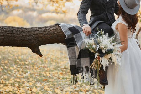 Téléchargez les photos : Mariée et marié baisers et tenant beau bouquet dans la nature en automne - en image libre de droit