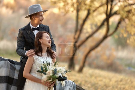 Foto de Hermosa feliz novia y novio con estilo en el sombrero cerca del árbol en otoño - Imagen libre de derechos