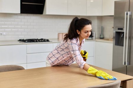 Photo for Young woman cleaning and wiping wooden table with microfiber cloth. chores at home. Housekeeping - Royalty Free Image