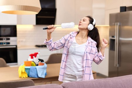 Téléchargez les photos : Jeune femme au foyer heureuse chantant et nettoyant sa maison, fille appréciant le travail domestique. - en image libre de droit
