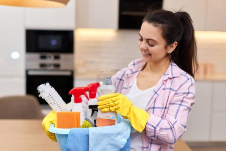 Photo for Woman in rubber protective yellow gloves holding bucket with cleaning detergents and rags . house chores. - Royalty Free Image