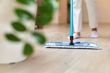 Photo for Young woman cleaning and mopping floor at living room, daily housekeeping , close-up - Royalty Free Image