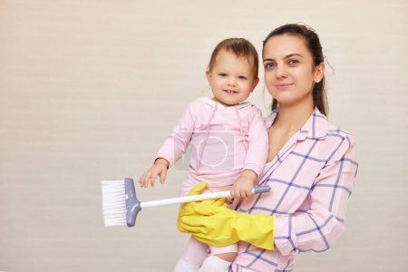 Téléchargez les photos : Mère souriante femme au foyer tient bébé fille mignonne et faire des travaux ménagers à la maison, famille heureuse, espace de copie - en image libre de droit