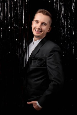 Téléchargez les photos : Joyeux bel homme en veste noire souriant sur fond de paillettes. - en image libre de droit