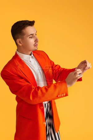 Téléchargez les photos : Joyeux jeune homme drôle en veste orange et pantalon rayé sur fond jaune. - en image libre de droit