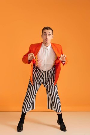 Téléchargez les photos : Jeune homme drôle extravagant en veste orange et pantalon rayé sur fond jaune. - en image libre de droit