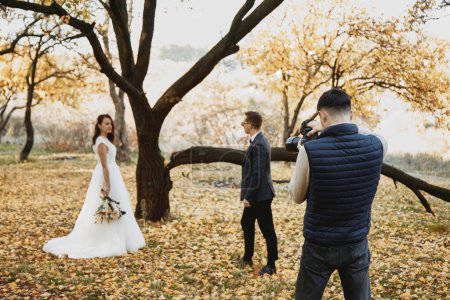 Foto de Fotógrafo de bodas profesional tomando fotos de la novia y el novio en la naturaleza en otoño - Imagen libre de derechos