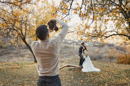 Téléchargez les photos : Photographe de mariage professionnel prenant des photos de la mariée et le marié dans la nature en automne - en image libre de droit