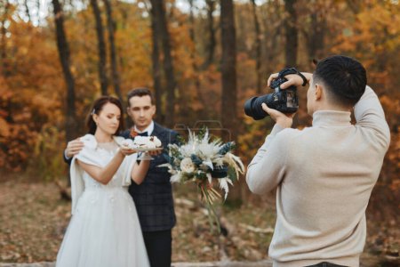 Téléchargez les photos : Photographe de mariage professionnel prenant des photos de la mariée et le marié dans la nature en automne - en image libre de droit
