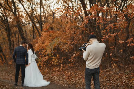 Foto de Fotógrafo de bodas profesional tomando fotos de la novia y el novio en la naturaleza en otoño - Imagen libre de derechos