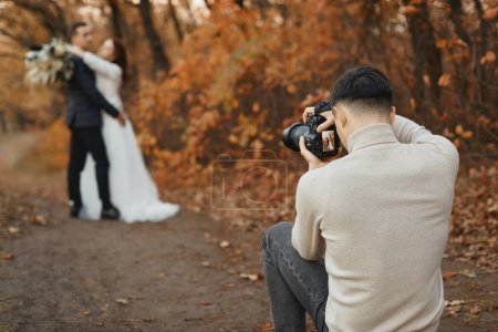 Téléchargez les photos : Photographe de mariage professionnel en action. les mariés dans la nature en automne - en image libre de droit