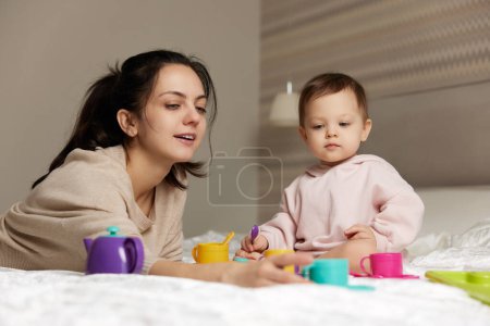Téléchargez les photos : Mère et petite fille enfant jouant au thé et passant du temps ensemble dans la chambre à coucher, famille s'amusant, - en image libre de droit