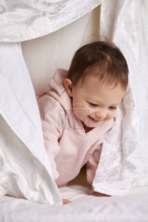 Photo for Cute funny little child girl looks out from under the blanket on the bed - Royalty Free Image