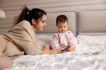 Téléchargez les photos : Jolie mère jouer puzzle avec son petit enfant fille dans chambre - en image libre de droit