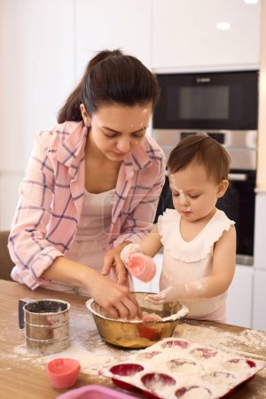 Photo for Mother and little baby girl preparing the dough in the kitchen, bake cookies. happy time together - Royalty Free Image