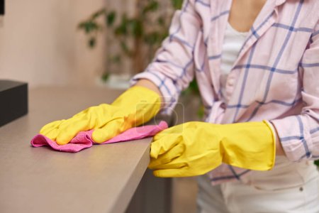 Téléchargez les photos : Jeune femme en gants de nettoyage et d'essuyage table avec chiffon en microfibre. corvées à la maison. Ménage - en image libre de droit