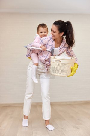 Photo for Happy mother housewife is holding cute baby girl and basket with laundry , Happy family - Royalty Free Image