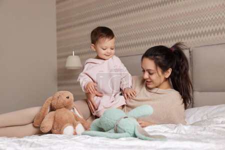 feliz madre y su hija pequeña jugando con juguetes de conejito en el dormitorio, la familia se divierte
