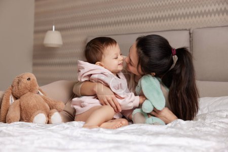 Foto de Feliz madre y su hija pequeña jugando con juguetes de conejito en el dormitorio, la familia se divierte - Imagen libre de derechos
